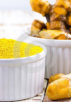 turmeric powder, saffron roots in wooden bowl on white table