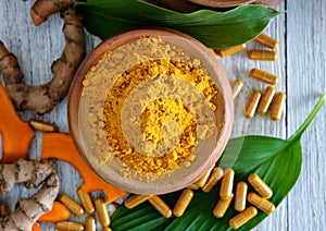 Turmeric powder and turmeric capsules on wooden background