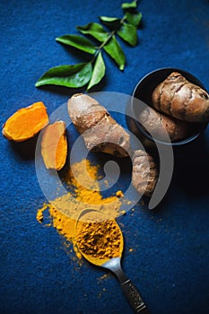 Turmeric Powder and Turmeric Root on a blue background, with curry leaves. Top View of auspicious indian spice haldi