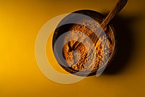 Turmeric powder in wooden bowl with wooden spoon on yellow background. Closeup view. Low key image with copy space photo