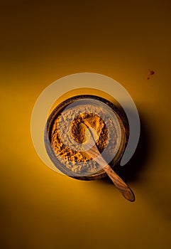 Turmeric powder in wooden bowl with wooden spoon on yellow background. Top view. Low key image with copy space photo
