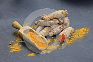 Turmeric powder in a wooden spoon and roots on a dark table curcuma longa, Kurkuma