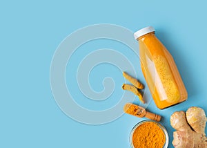 Turmeric smoothie in glass bottle with ingredients, turmeric powder on blue background