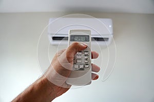 Turn on the air conditioner at 25 degrees Celsius. Hand holding the air conditioner remote control and thumb is pressing a button
