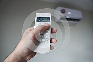 Turn on the air conditioner at 26 degrees Celsius. Hand holding the air conditioner remote control and thumb is pressing a button
