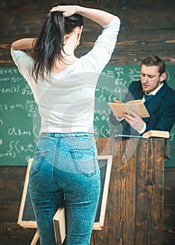 Turn back girl making a ponytail while holding a book between her legs. Young student rear view. Professor reading from