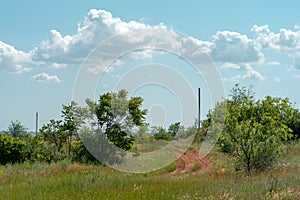 Turn of a dirt country road in the field, against the background of the summer blue sky. Beautiful countryside landscape