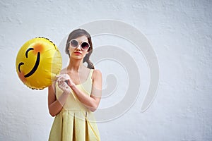 Turn that frown upside down. Studio portrait of a confident young woman holding a smiling emoticon balloon while