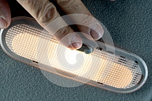 Turn on the lamp with the button. Closeup photo of hands man turning light on in car salon