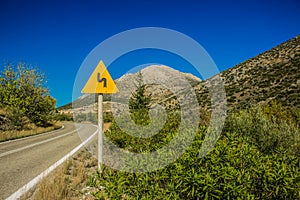 Turn left sign on empty curved car road in highland mountain rocky country environment