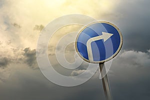 Turn right ahead sign, blue round roadside traffic signage, against the dramatic sky