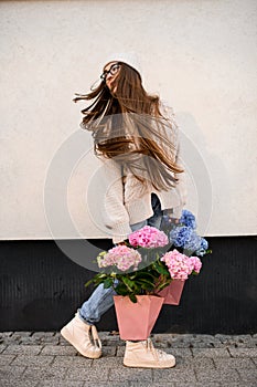 Turned around girl in a hat and jeans with pink and blue bouquets in the hands