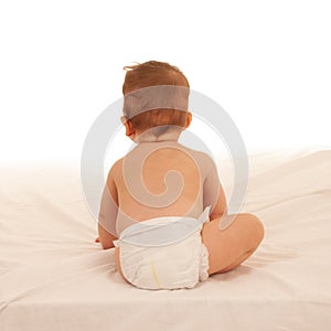 Turned away baby plays on bed isolated over white background