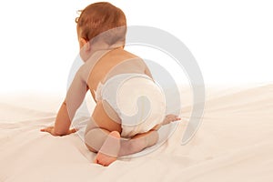 Turned away baby plays on bed isolated over white background