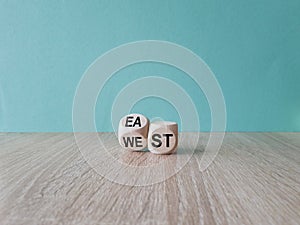Turned a cube and changes the word east to west, or vice versa. Beautiful wooden table, blue background, copy space. Business
