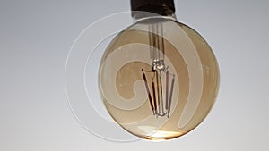 Turned off round electric light bulb with dark glass is hanging on white ceiling. Stylish detail of design interior