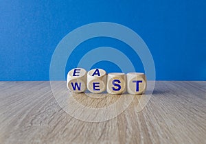 Turned wooden cubes and changes the word east to west, or vice versa. Beautiful wooden table, blue background, copy space.