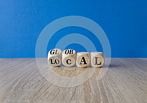 Turned wooden cubes and changes the word local to global. Beautiful wooden table, blue background. Business and local or global