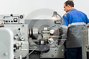 Turner stands behind lathe in production hall and works. View of worker from behind from back in overalls.