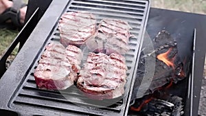 Turning beef steaks grilling on a cast iron plate on a camp fire. Campfire cooking. Outdoor BBQ.