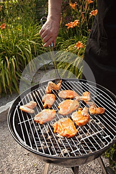Turning chicken wings and steaks on a barbeque grill.