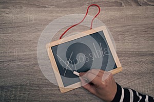 Turning the impossible into the possible. Impossible written with white chalk on a blackboard in woman's hands