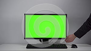 Turning on the monitor with a green screen. A man with his hand turns on the computer screen on the desktop in the