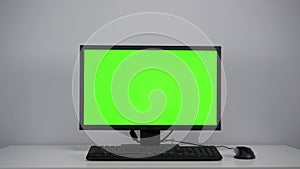 Turning on the monitor with a green screen. A man with his hand turns on the computer screen on the desktop in the