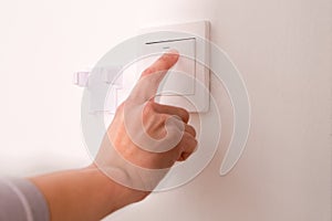 Turning off/on the wall-mounted electric light switch.