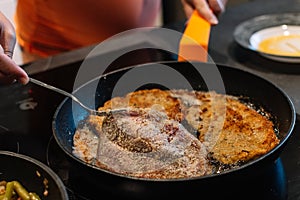 Turning over a piece of breaded pork in the pan for dinner