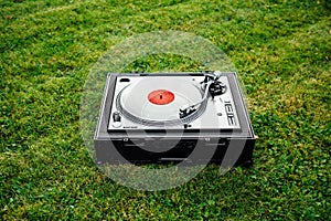 Turntable with LP vinyl record on grass background