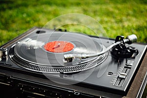 Turntable with LP vinyl record on grass background