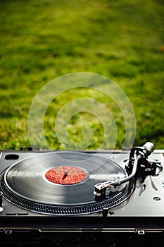 Turntable with LP vinyl record on grass background