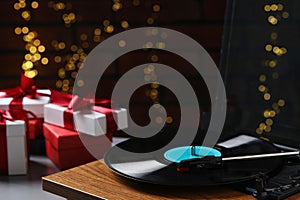 Turntable with vinyl record and Christmas gift boxes against blurred lights, closeup. Space for text
