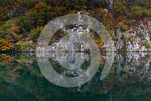 Turquoise blue mountain lake with reflections of cliffs and forest in intense fall colors