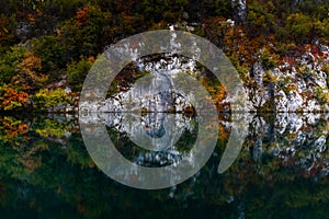 Turquoise blue mountain lake with reflections of cliffs and forest in intense fall colors