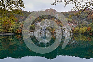 Turquoise blue mountain lake with reflections of cliffs and forest in intense fall colors