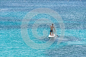 Turquoise-blue sea with a young man on a paddle board.