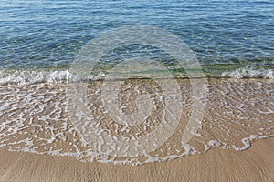 Turquoise foamy wave on a golden sandy shore. The calm surface of the sea. Relax and tranquility. Background. Space for text