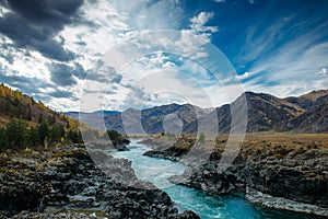 Turquoise Katun river in gorge is surrounded by high mountains under majestic autumn sky. A stormy mountain stream runs