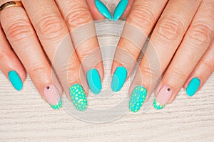 Turquoise nail art female manicure on a light wooden background. Long almond-shaped nails.
