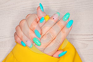 Turquoise nail art female manicure on a light wooden background. Long almond-shaped nails.