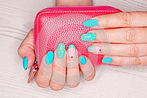 Turquoise nail art female manicure on a light wooden background. Long almond-shaped nails.