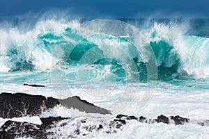 Turquoise rolling wave slaming on the rocks