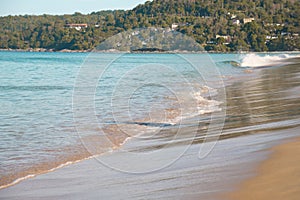 Turquoise sea wave rolls onto the flat, gently sloping shore of the sandy beach