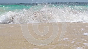 Turquoise sea waves splashing on sandy beach on blue skyline landscape. Ocean waves splashing on sandy beach on horizon