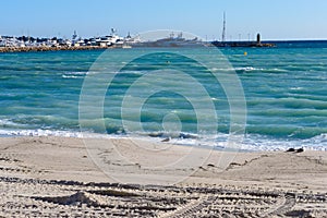 Turquoise sea, white yachts, lighthouse and footprints in the sand on a sunny day.