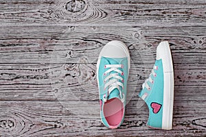 Turquoise sneakers with embroidered heart on the wooden floor. Sports style. Flat lay.