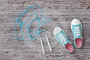 Turquoise sneakers and a high-speed jump rope on the wooden floor. Sports style. Flat lay.