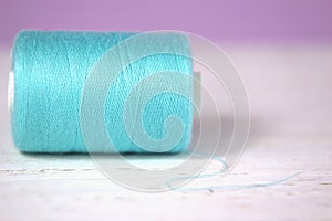 Turquoise thread on a lilac and white background